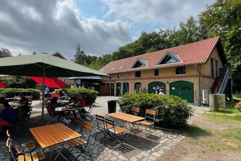 An outdoor seating area with tables and chairs, a covered umbrella, and a building with a red-tiled roof.