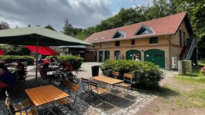 An outdoor seating area with tables and chairs, a covered umbrella, and a building with a red-tiled roof. - Holiday apartment Pahl (Ostseeheilbad Zingst)