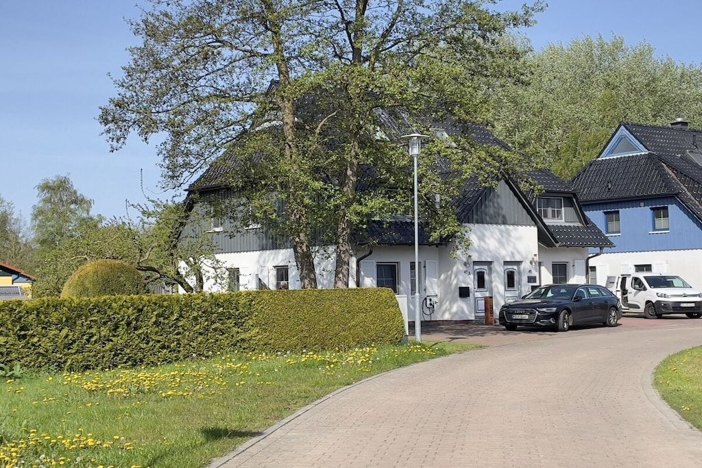 A residential area with a paved driveway leading to a house with a dark roof and white walls.