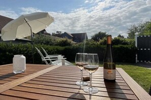 Een houten tafel met een fles wijn, twee glazen, een paraplu en een zoutvaatje.