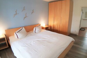 Une chambre à coucher comprenant un lit, une armoire en bois, des tables de chevet et des œuvres d’art murales.