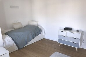 Ein Schlafzimmer mit einem Bett, Nachttisch, Schminktisch und einer Steckdose an der Wand.