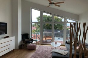 Ein modernes Wohnzimmer mit einer großen Schiebetür aus Glas, einem Deckenventilator, einem Flachbildfernseher, einem Sofa, einem Couchtisch und einem Sessel.