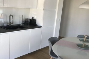 Eine moderne Küche mit weißen Schränken, einer schwarzen Arbeitsplatte und einem Spülbecken. Es steht ein kleiner Tisch mit Glasplatte und zwei Stühlen dort.