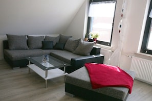 Ein modernes Wohnzimmer mit einem Ecksofa, einem Glastisch und einer roten Decke.