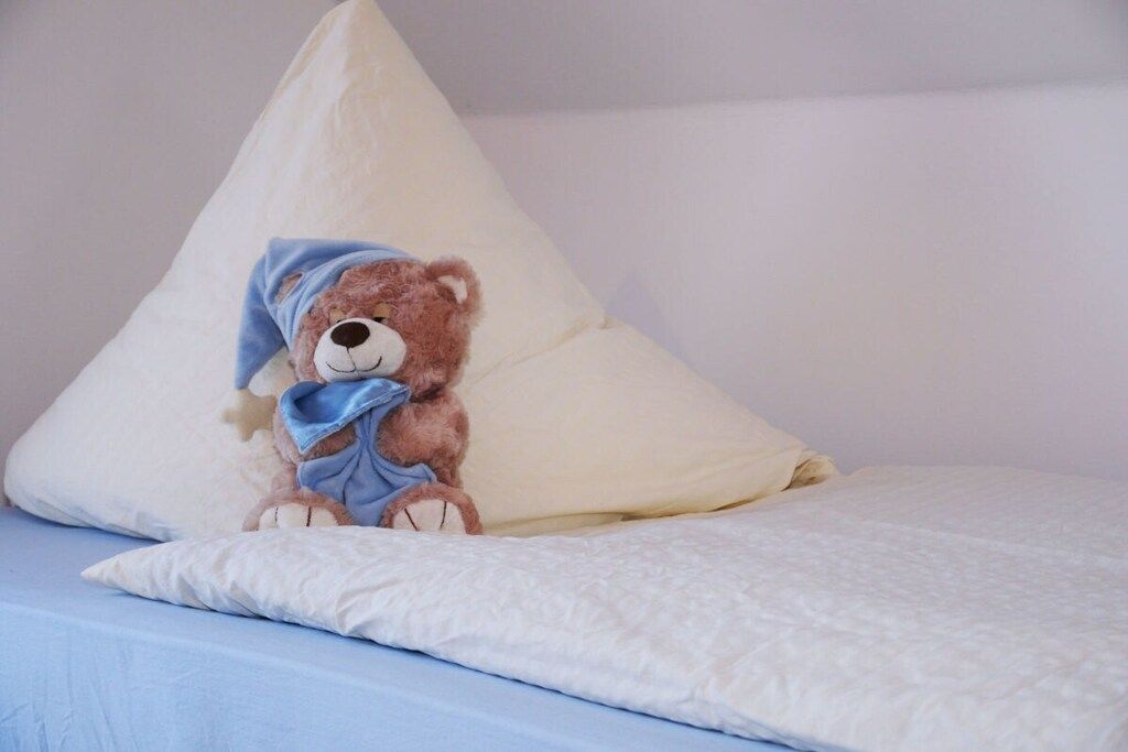 Un lit avec un oreiller blanc et un ours en peluche.