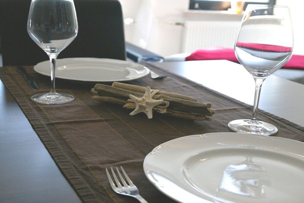 Une table à manger dressée avec des assiettes, des couverts et des verres, agrémentée d’une décoration en forme d’étoile de mer et de bâtons de cannelle.