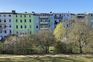 Une rangée d’immeubles résidentiels à plusieurs étages, dotés de balcons, est entourée d’un parc arboré sous un ciel dégagé.