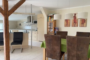 Un coin repas avec une table dressée pour quatre personnes, une cuisine en arrière-plan et une bibliothèque remplie de livres.
