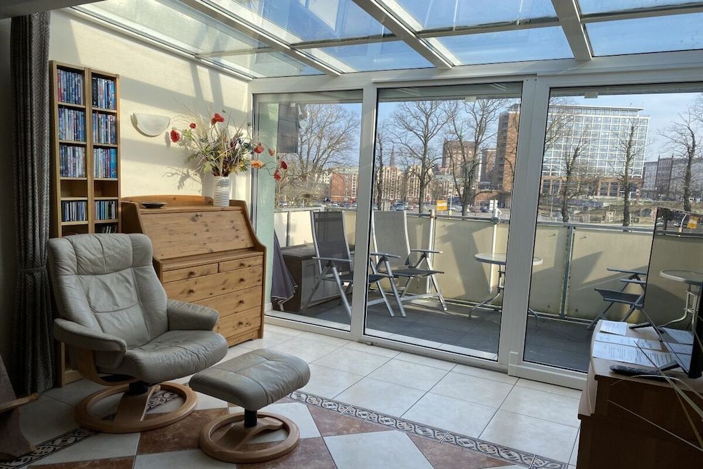 A modern room with a glass ceiling, a comfortable chair, a wooden bookshelf, and a view of the cityscape.