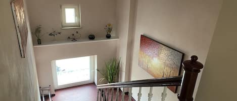 A staircase with a wooden handrail and white balusters, leading to a landing with a window and a shelf with decorative items.