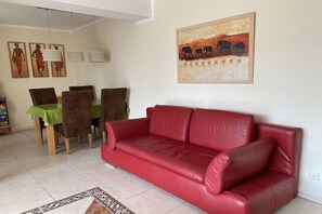 Ein Wohnzimmer mit einem roten Ledersofa, einem Essbereich mit einem grünen Tisch und Stühlen sowie einem Elefantenbild an der Wand.