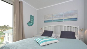 A bedroom with a bed, a headboard, a window with curtains, a wall-mounted sign, and a painting. - Holiday apartment in Glowe with swimming pool (Glowe)