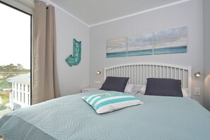 A bedroom with a bed, a headboard, a window with curtains, a wall-mounted sign, and a painting. - Holiday apartment in Glowe with swimming pool (Glowe)