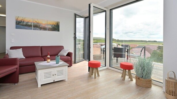 A modern living room with a red sofa, a white coffee table, and two red stools. - Holiday apartment in Glowe with swimming pool (Glowe)
