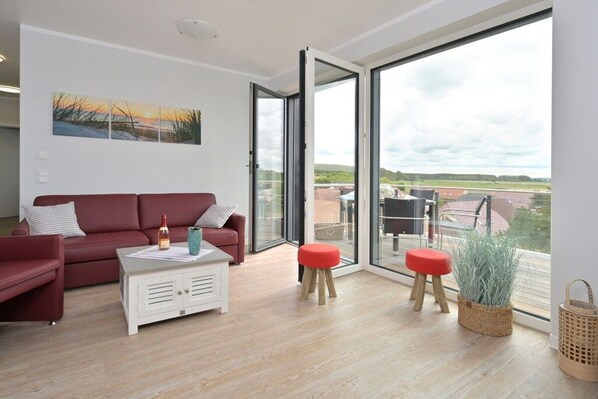 A modern living room with a red sofa, a white coffee table, and two red stools. - Holiday apartment in Glowe with swimming pool (Glowe)