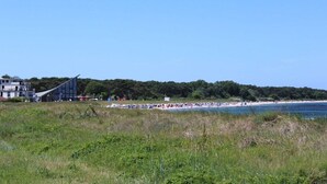 A coastal area with a beach, a building with a sloped roof, and a forested hill in the background. - Holiday apartment in Glowe with swimming pool (Glowe)