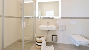 A bathroom with a glass shower enclosure, a sink, a toilet, and a trash can. - Holiday apartment in Glowe with swimming pool (Glowe)