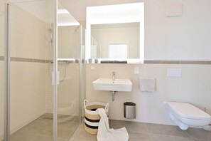 A bathroom with a glass shower enclosure, a sink, a toilet, and a trash can. - Holiday apartment in Glowe with swimming pool (Glowe)