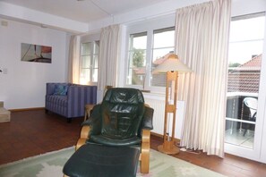 A living room with a leather chair, a sofa, a lamp, and a view through a window. - Angelika's holiday apartment Prerow (Prerow)