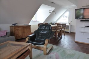 A modern living room with a black leather chair, wooden furniture, a dining area, and a flat-screen TV mounted on the wall. - Angelika's holiday apartment Prerow (Prerow)