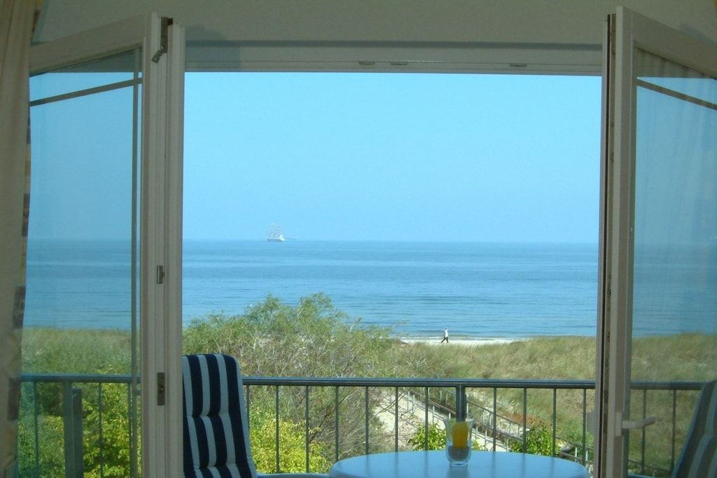A balcony with a table and chairs, overlooking a beach and the sea.