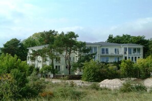 Ein zweistöckiges Gebäude mit flachem Dach, umgeben von üppigem Grün und Bäumen.