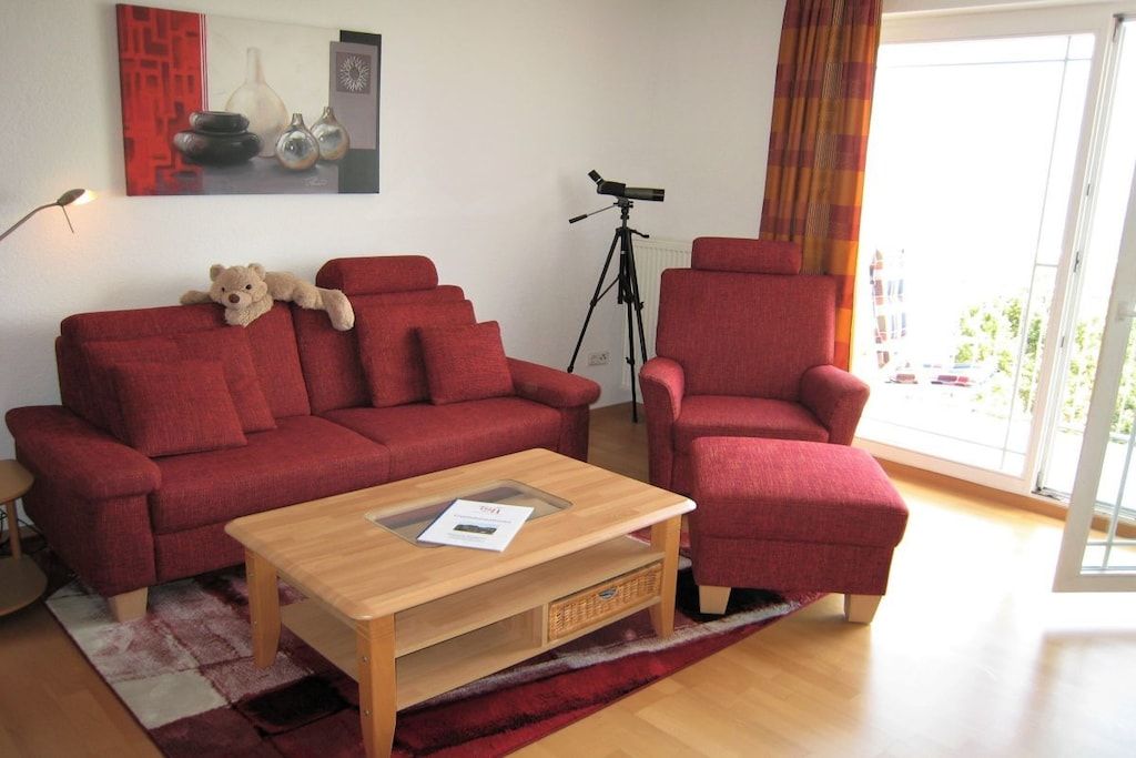 Een woonkamer met een rode bank, een rode fauteuil, een houten salontafel en een telescoop tegen de muur.