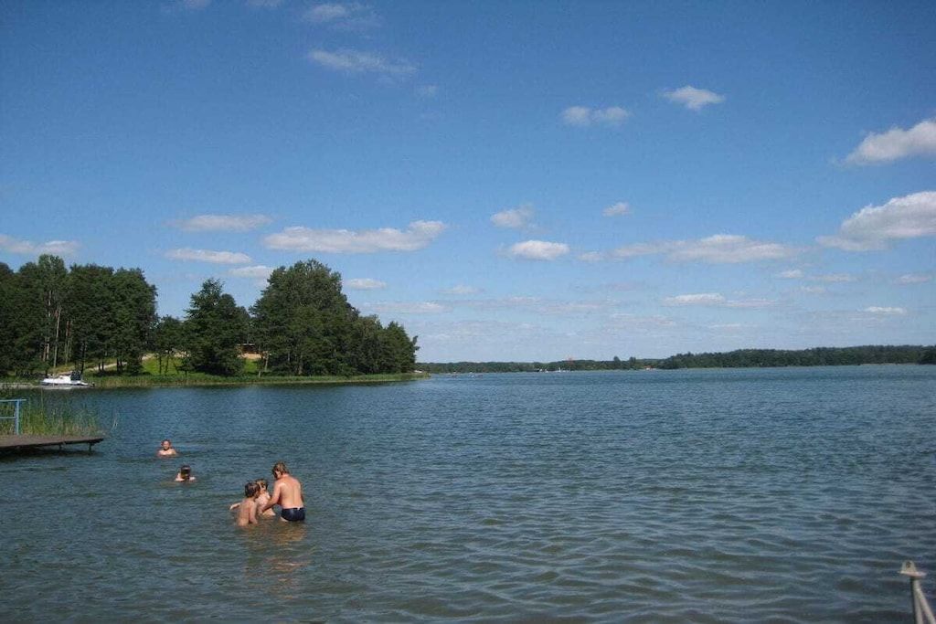 Ein See mit Schwimmern, einem Steg und Bäumen im Hintergrund.