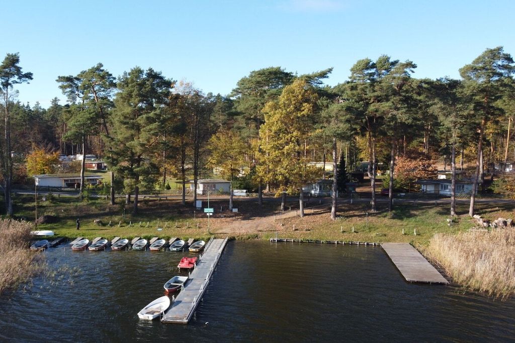 A dock with boats, a small pier, and a forested area with cabins in the background.