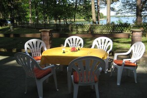 An outdoor dining area with a round table and white chairs, set against a backdrop of trees and a body of water. - Holiday park in Lychen with swimming pool (Lychen)
