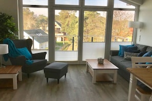 Ein Wohnzimmer mit großem Fenster, einer Couch, einem Couchtisch und einem Sessel.