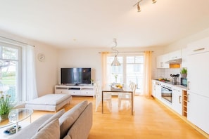 Een moderne woonkamer met een bank, een televisie en een eethoek met een tafel en stoelen.