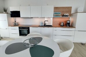 A modern kitchen with white cabinetry, a built-in oven, a coffee maker, and a toaster on the countertop. - Holiday apartment in Glowe with swimming pool (Glowe)
