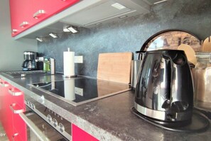Una cuina moderna amb fogó d'acer inoxidable, cafetera i bullidora.