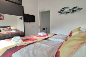 A hotel room with two beds, a flat-screen TV mounted on the wall, and a door leading to another room. - Holiday apartment in Glowe with swimming pool (Glowe)