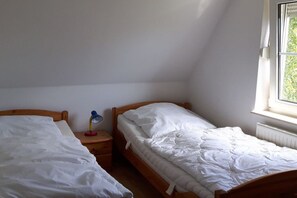 A bedroom with two single beds, a nightstand with a lamp, and a window providing natural light. - Holiday apartment in Breege with Wi-Fi (Breege)