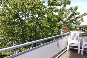 A balcony with a railing, a white plastic chair, and a tree with green leaves. - Holiday apartment in Breege with Wi-Fi (Breege)