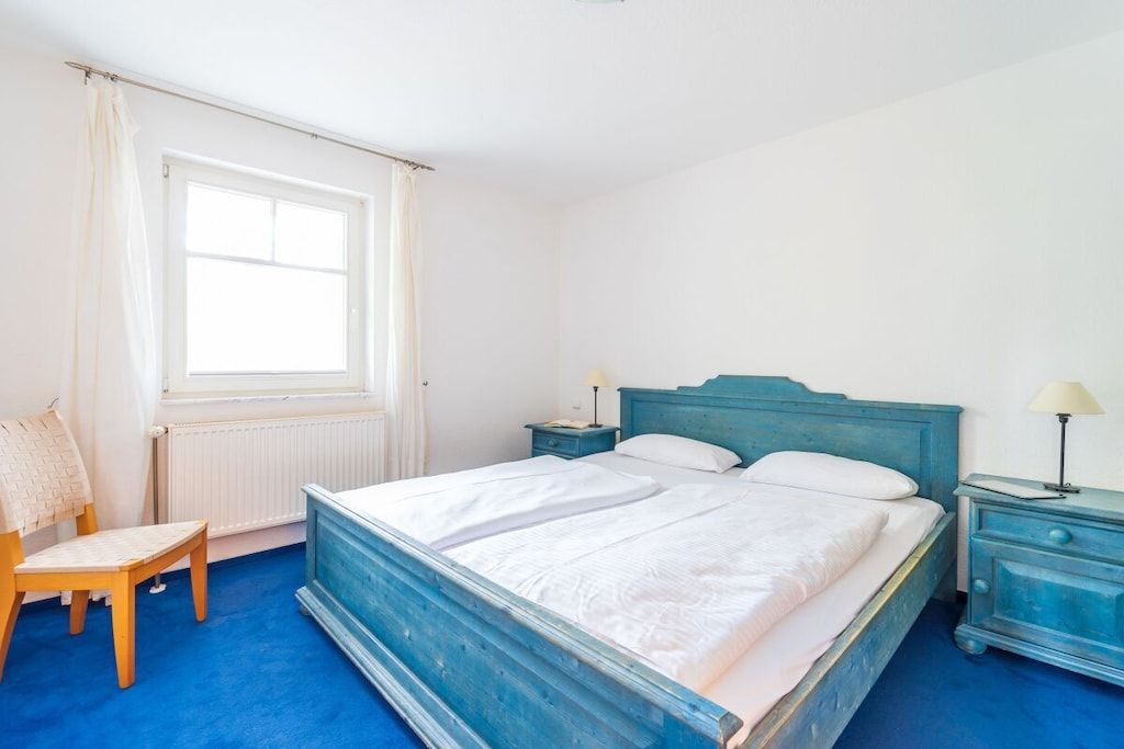 Ein Schlafzimmer mit einem Einzelbett, einem Sessel, einem Nachttisch und einem Fenster.