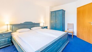 Un dormitori amb un llit, fallegueres, un armari de fusta, una cadira i una porta.