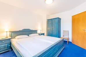 Een slaapkamer met een bed, nachtkastjes, een houten kledingkast, een stoel en een deur.