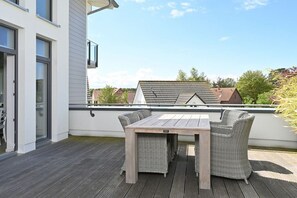 Een balkon met een houten tafel en rieten stoelen, met uitzicht op een woonwijk.