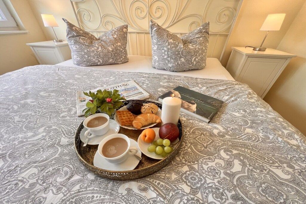 A neatly made bed with a patterned bedspread, two pillows, a tray with breakfast items, and a book on the bed.