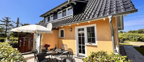 A two-story house with a tiled roof, a covered patio with outdoor furniture, and a garden.