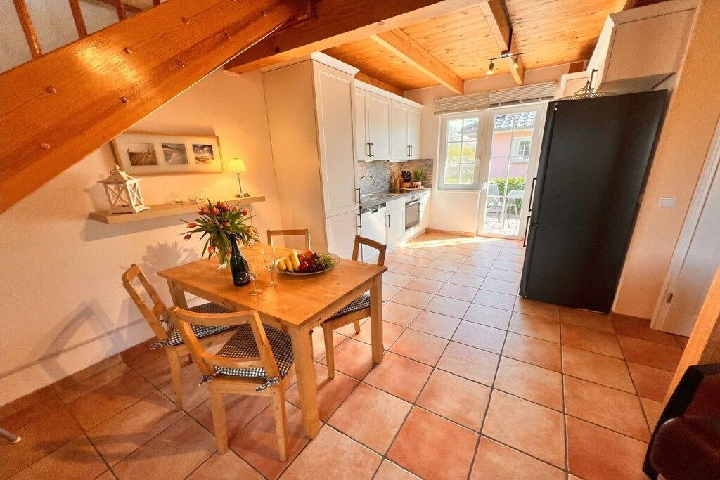 A dining area with a wooden table and chairs, a kitchen with white cabinets, and a black refrigerator.