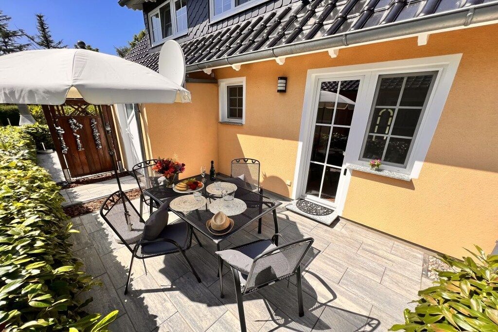 Eine Terrasse im Freien mit Tisch und Stühlen, einem weißen Sonnenschirm und einem Haus mit einem Ziegeldach.