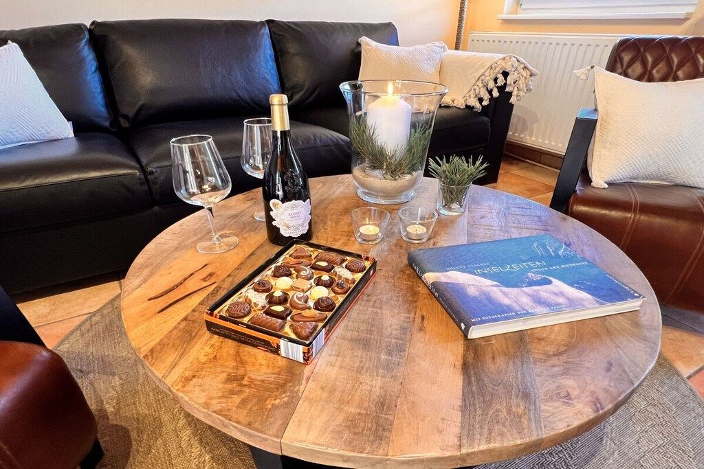 Een ronde houten tafel met een fles wijn, glazen, een kaars, een boek en een doos chocolade.