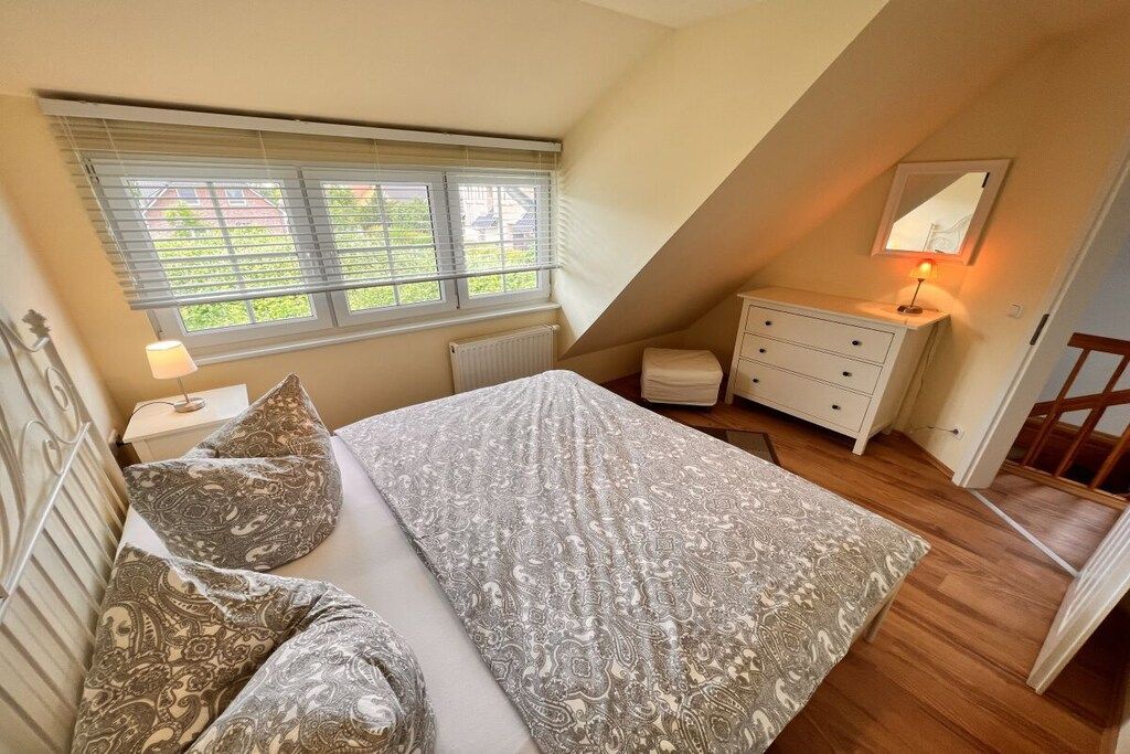 A bedroom with a bed, a dresser, a nightstand, a lamp, and a window with blinds.