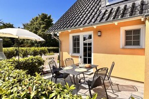 A patio with a table and chairs, a white umbrella, and a building with a tiled roof. - Holiday home in Rügen with 1 bedroom (Dranske-Lancken)