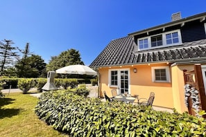 Una casa amb teulada de rajola, un porxo cobert amb cadires i un jardí ben cuidat.